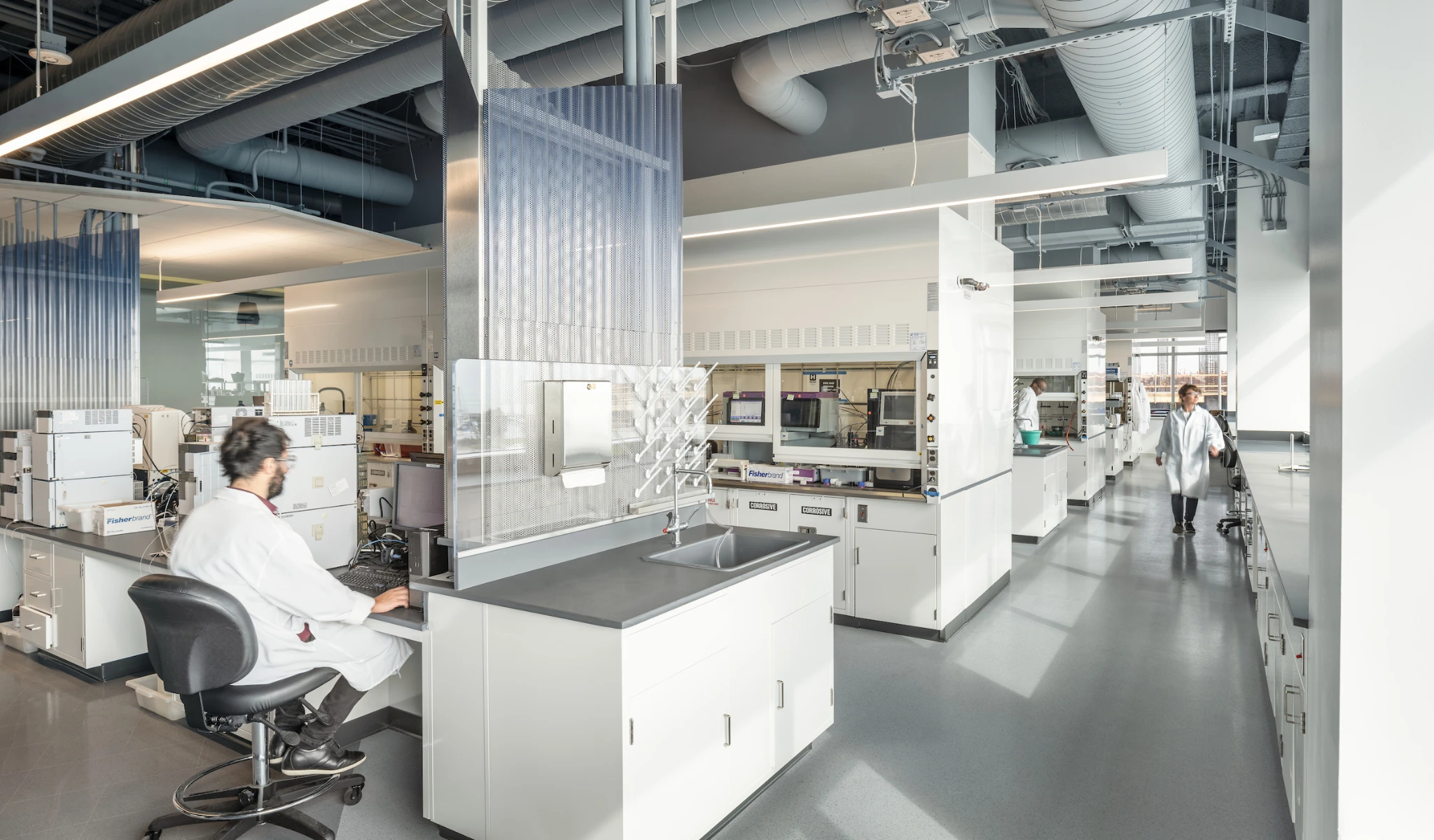 Modern laboratory with state-of-the-art equipment, showing a technician working at a computer station and other scientists in lab coats performing experiments in the background.