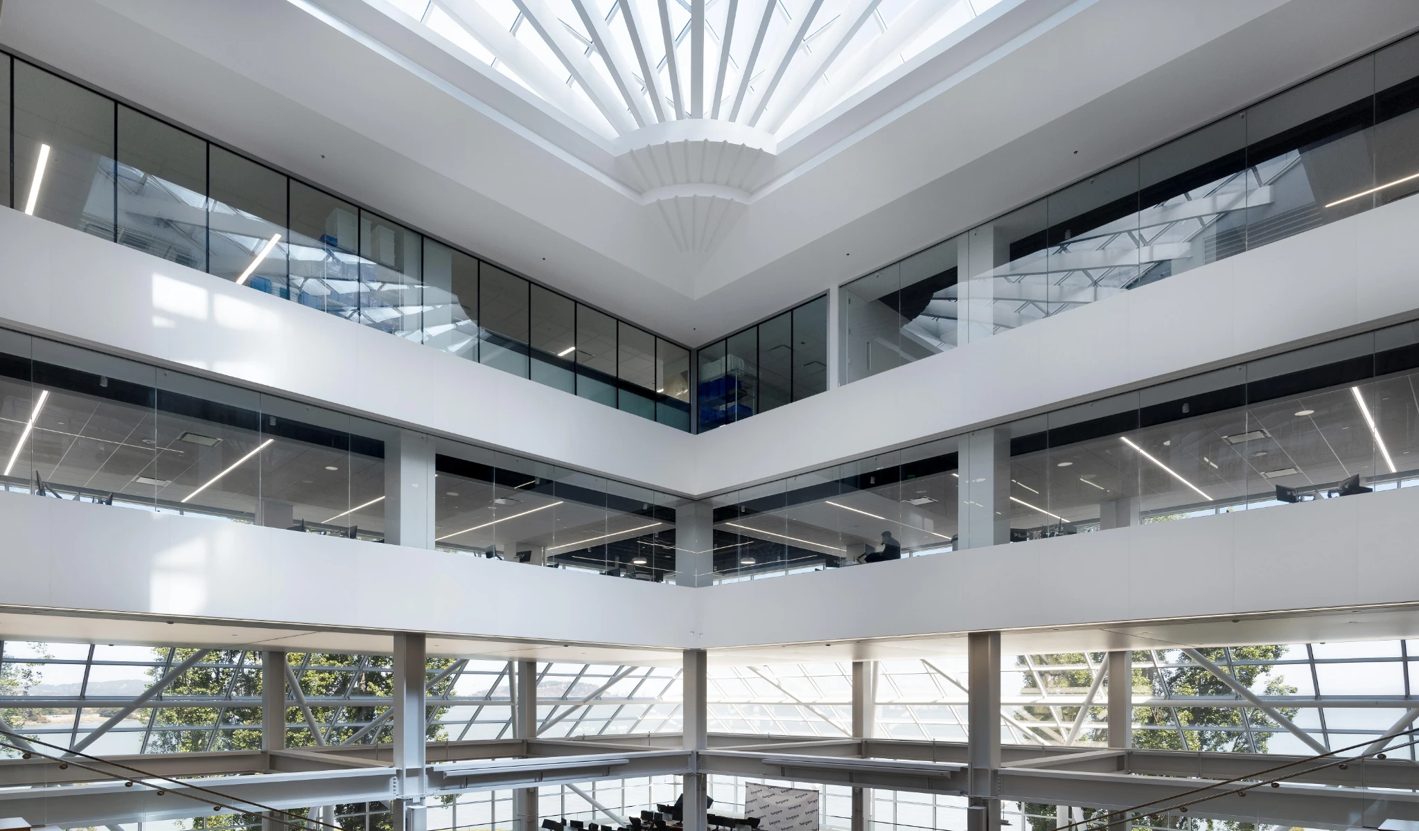 Modern, multi-story atrium with large windows, glass walls, and skylight, allowing natural light to illuminate the open space.
